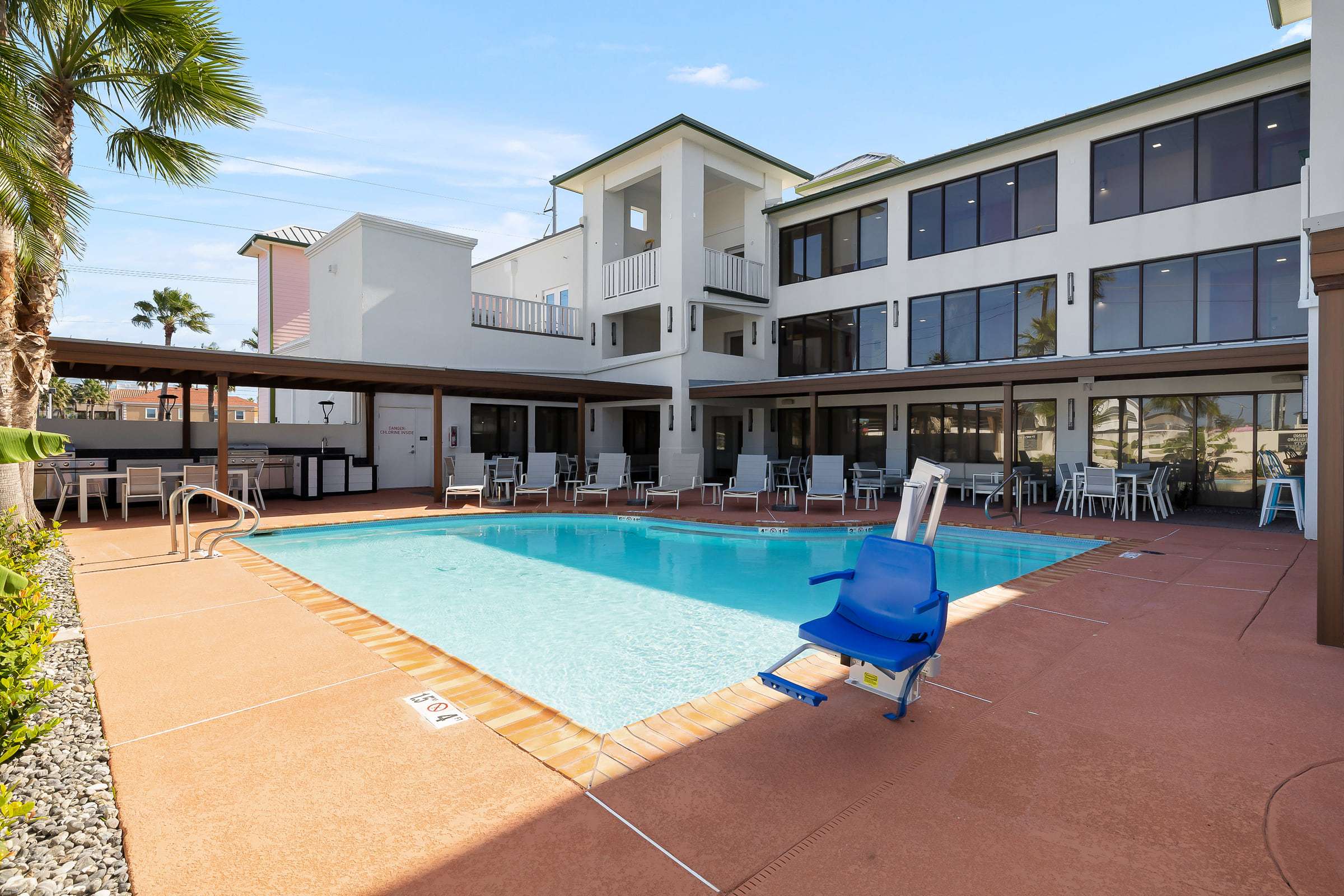 Outdoor pool with lounge chairs, accessible pool lift and covered patio with grills
