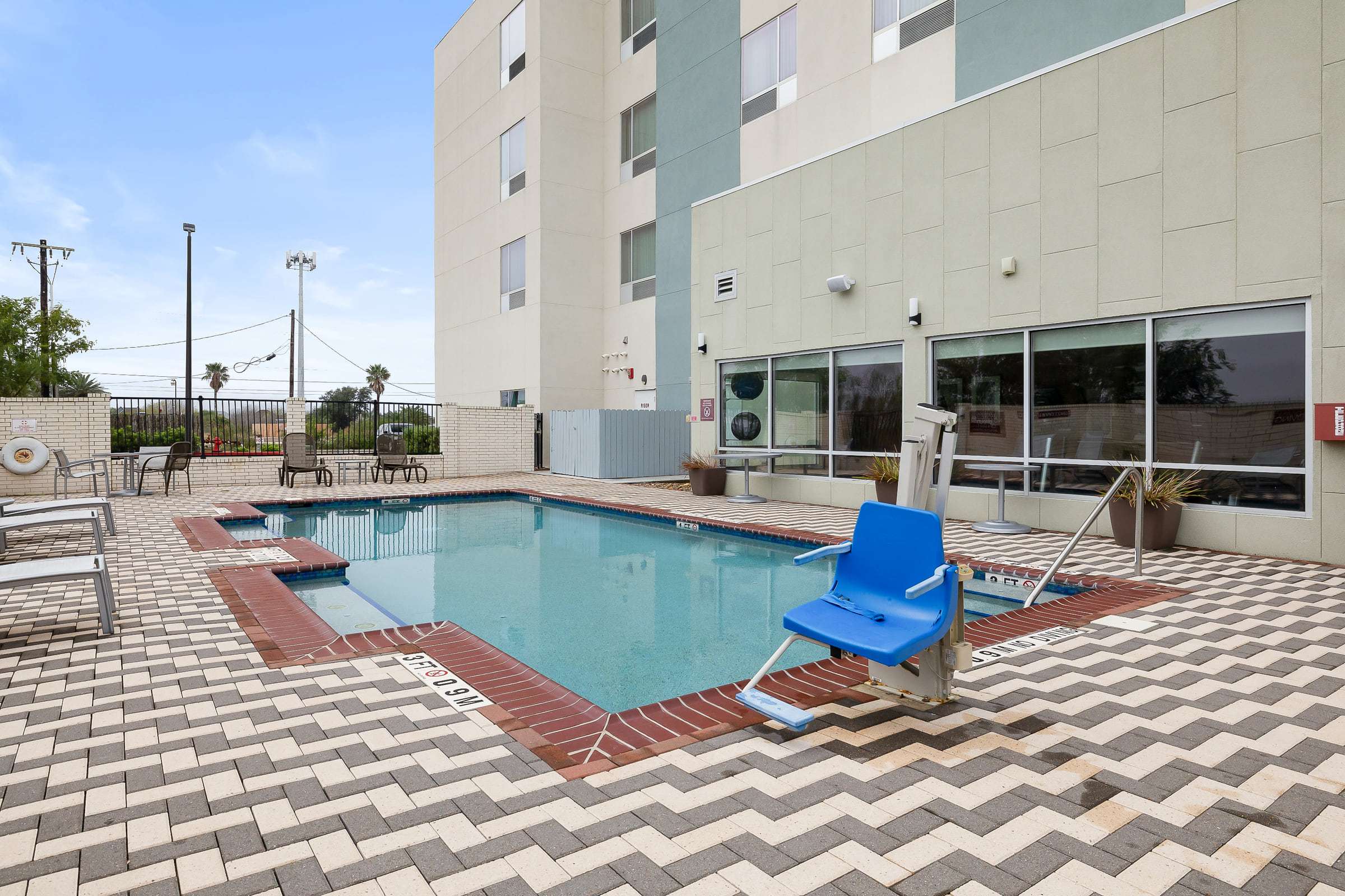 Outdoor pool with chevron paver deck, pool lift and lounge chairs beside the fitness center