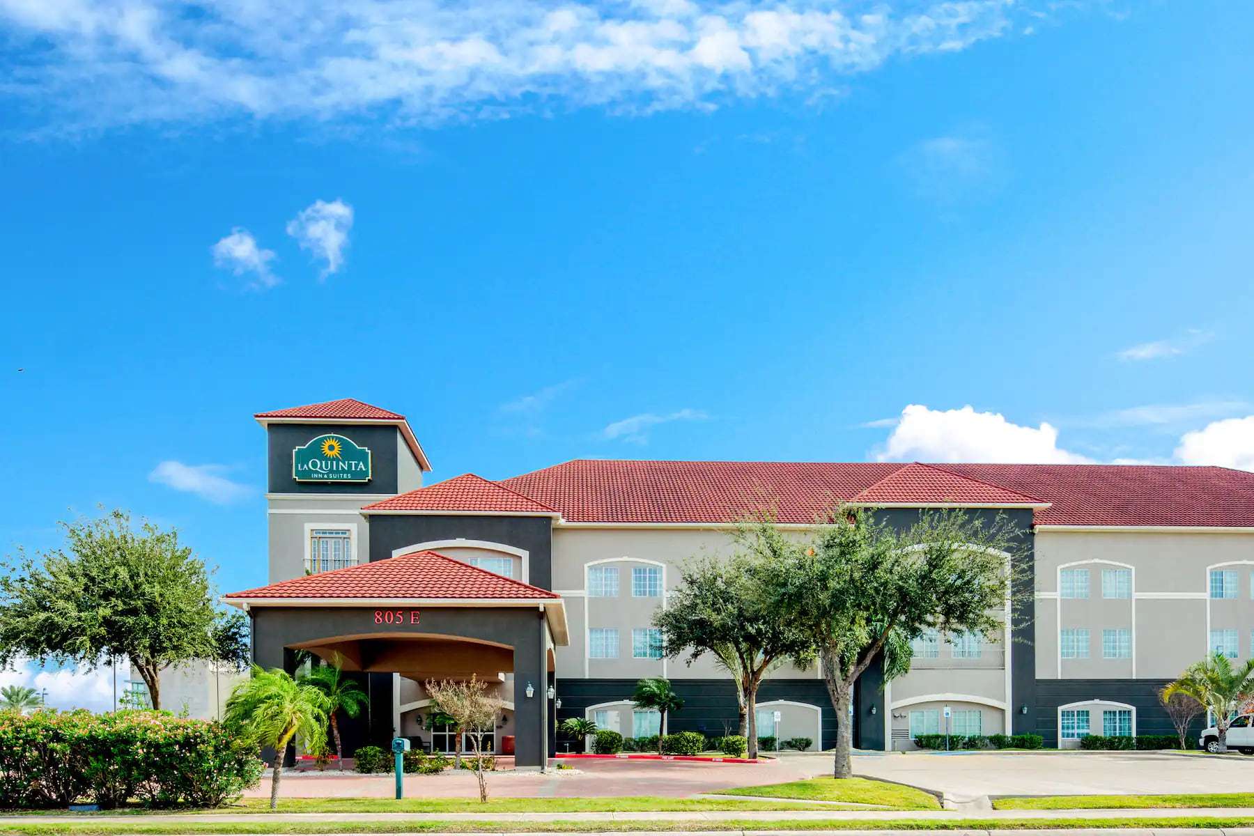 La Quinta Inn & Suites exterior by day with porte-cochere, red tile roof and palm trees