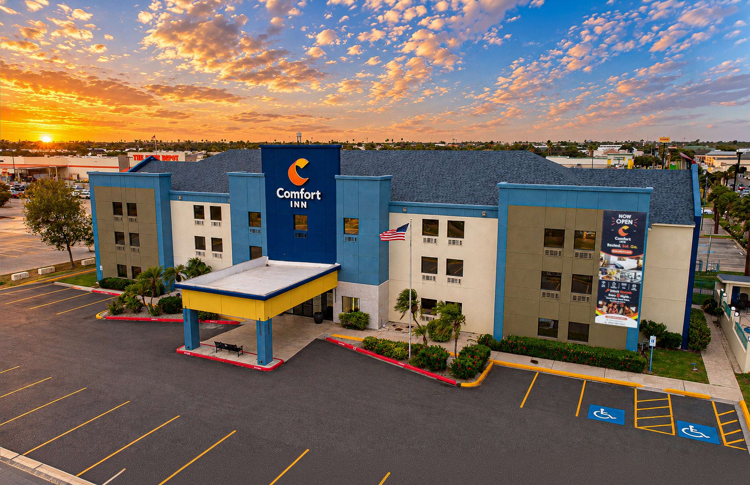 Aerial view of the three-story Comfort Inn, its yellow porte-cochère and parking lot under a sunset sky