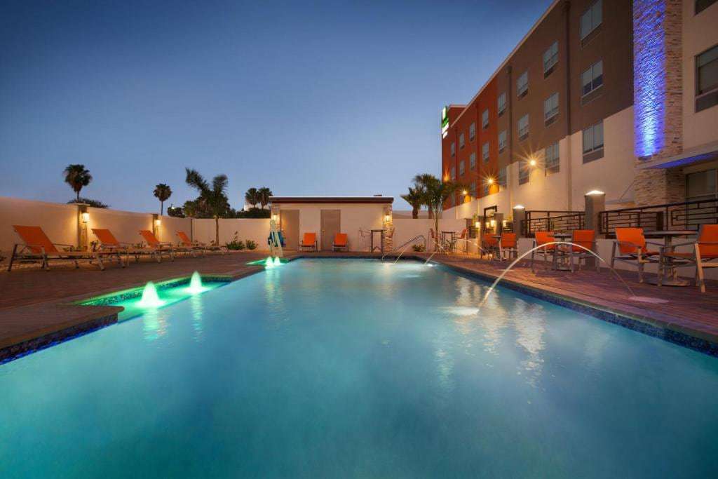 Outdoor pool at dusk with lit fountain jets, orange lounge chairs and patio tables beside the hotel