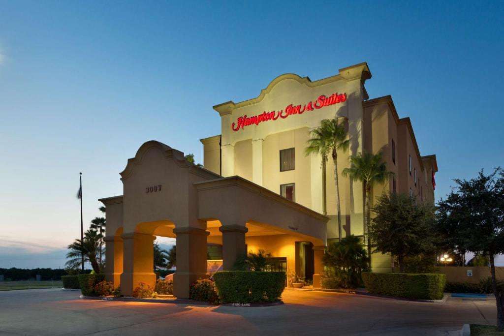 Hotel entrance with lit porte-cochere and red Hampton Inn & Suites sign at dusk