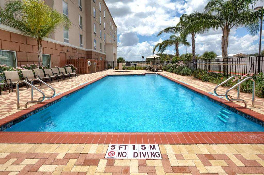 Outdoor pool with lounge chairs, palm trees and an umbrella table on a brick paver deck