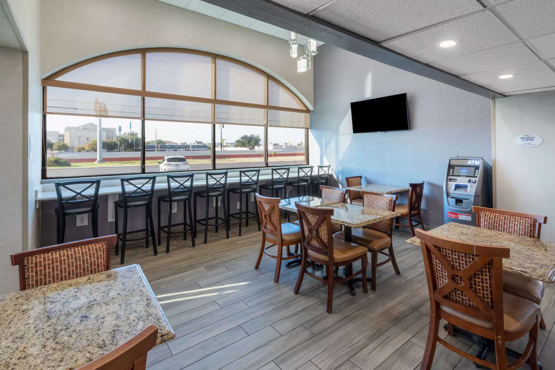 Lobby seating area with dining tables, window bar seating, wall TV and ATM
