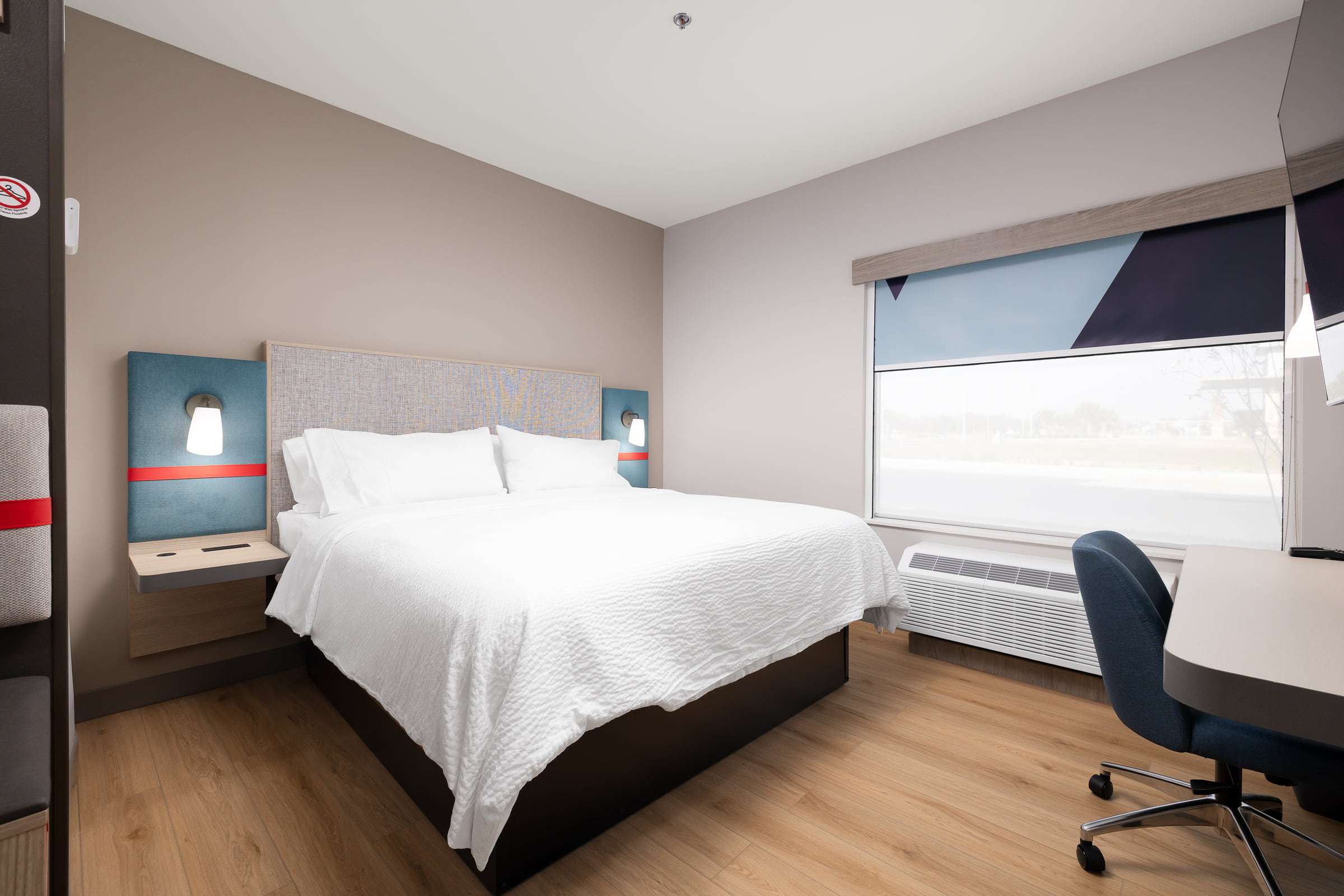 avid hotel king room with white bedding, wall reading lamps, work desk and large window