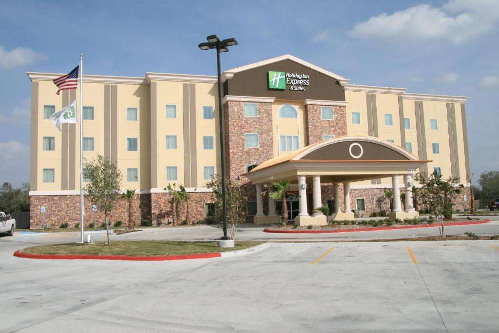 Hotel front with columned porte-cochere, flagpole and front parking lot under a blue sky