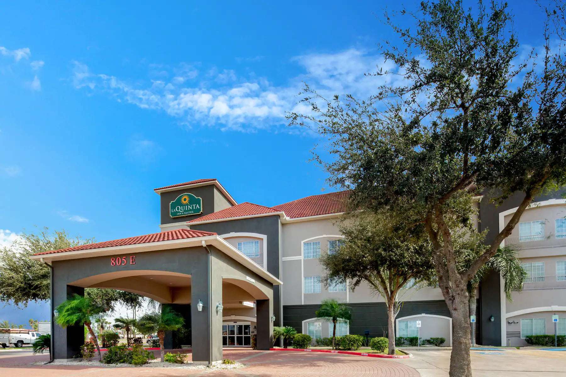 Hotel entrance porte-cochere marked 805 E under blue sky, framed by live oak trees