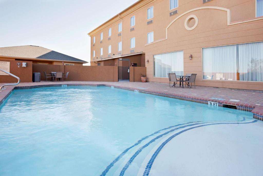 Outdoor pool with curved step entry, brick deck and patio tables beside the hotel