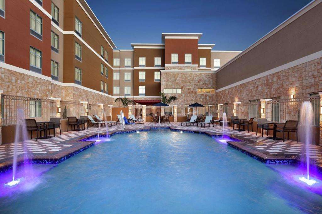 Courtyard outdoor pool at dusk with lit fountains, lounge chairs and patio tables
