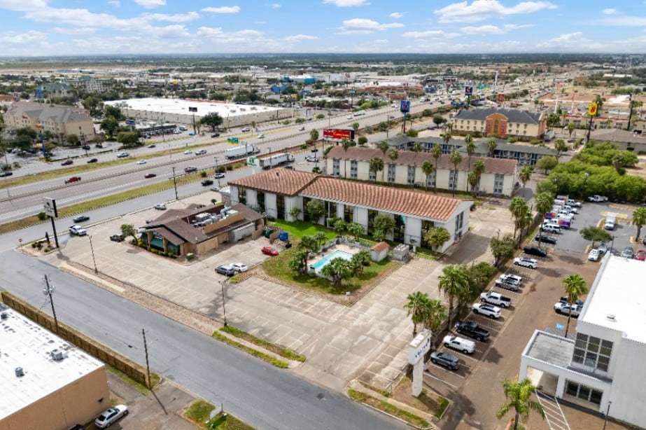 Aerial view of the area around the hotel with palm-lined lots, a courtyard pool and the highway
