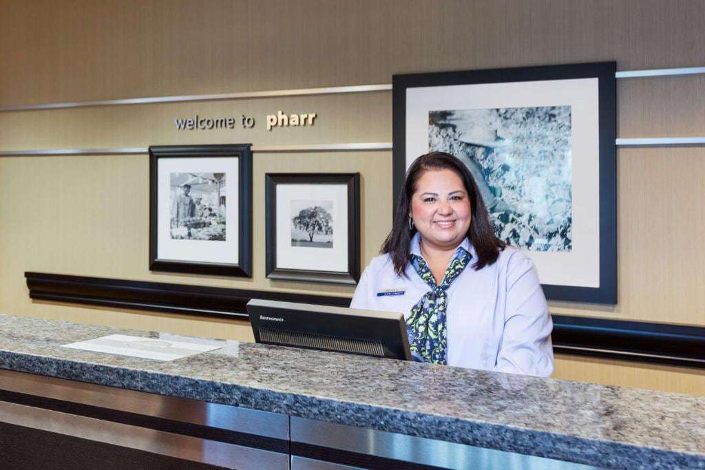 Front desk agent at the granite counter beneath a "Welcome to Pharr" sign