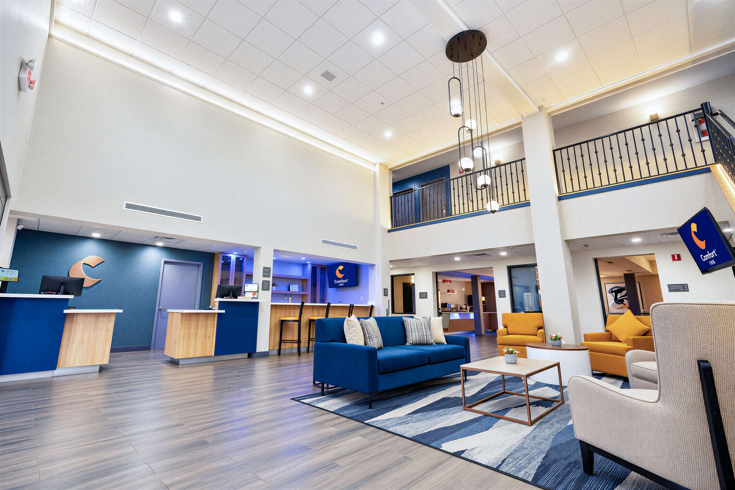 Two-story lobby with a front desk, copper C logo, blue sofa, armchairs and a pendant light below a mezzanine