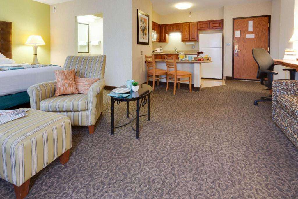 Suite sitting area with armchair, sofa and desk next to a kitchenette with full-size fridge and breakfast bar
