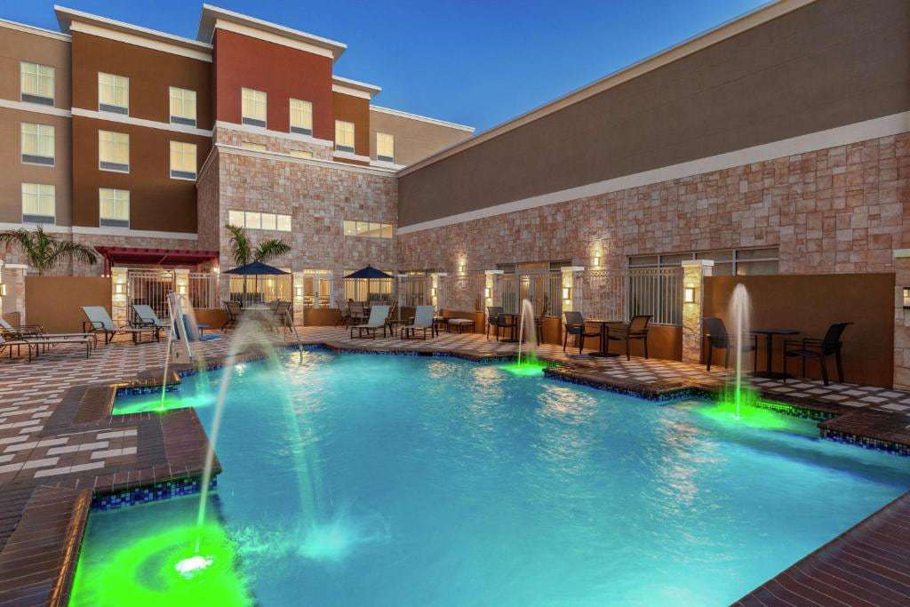 Outdoor pool with lit water jets, umbrellas and lounge chairs beside the stone facade