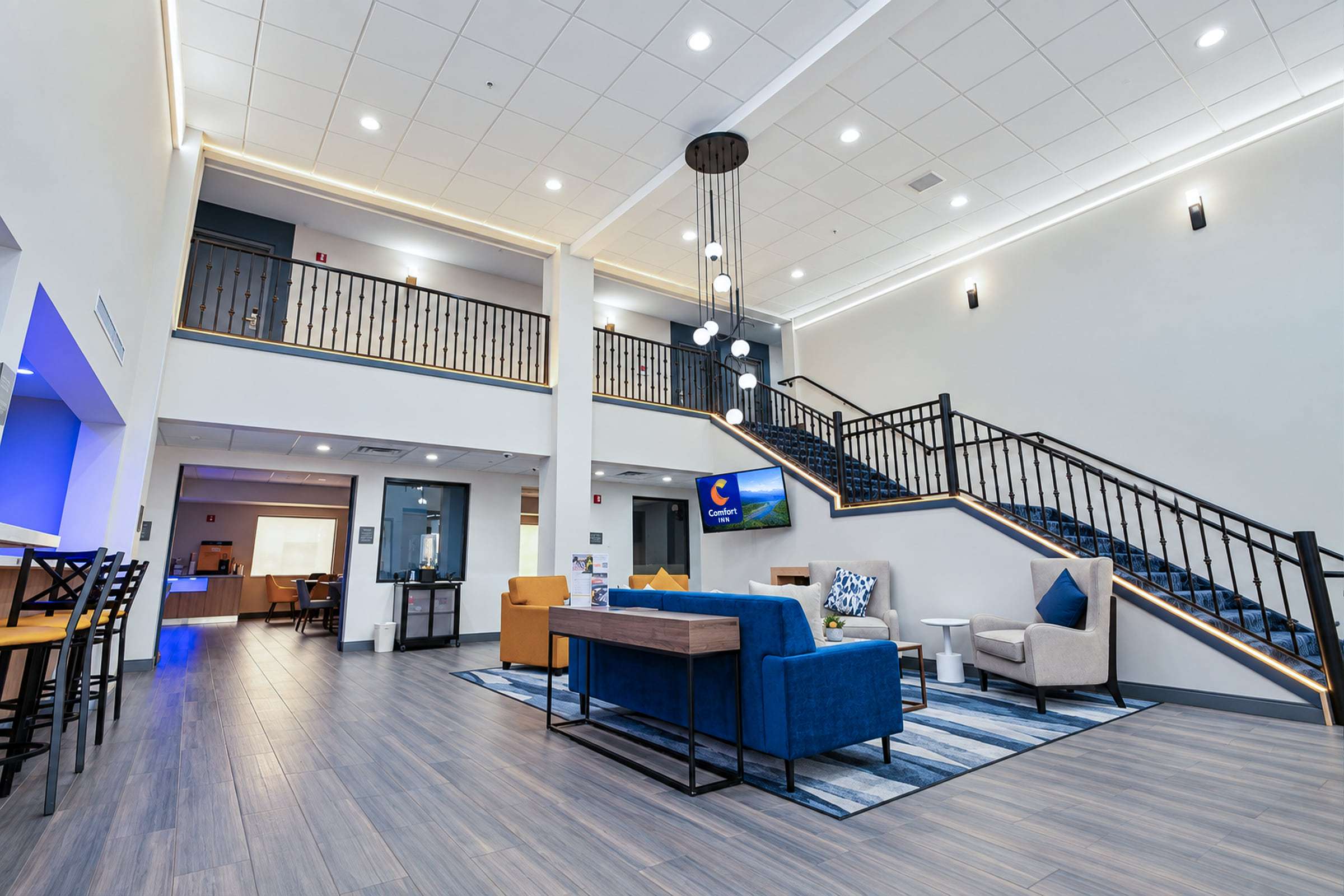 Lobby seating area with a blue sofa, yellow and cream armchairs, a pendant light and a carpeted staircase