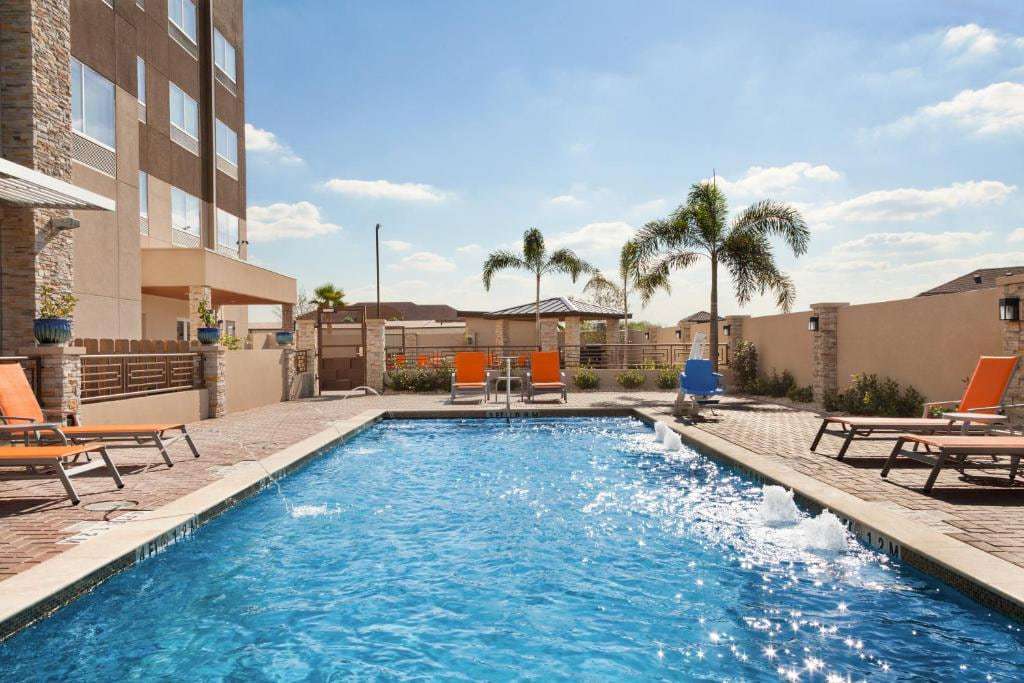 Outdoor pool with fountain jets, orange lounge chairs, palm trees and a stone-pillar gazebo