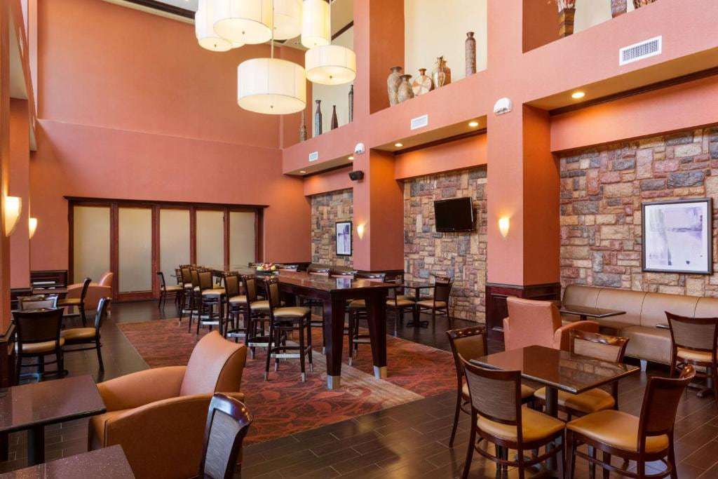 Two-story lobby lounge with high-top table, dining tables, armchairs, sofa and stone accent walls