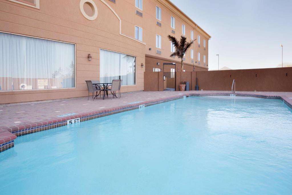 Walled outdoor pool with brick deck and a patio table set beside the hotel's stucco wing