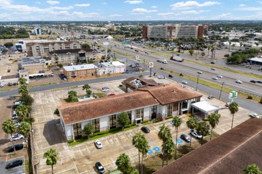 Aerial view over palm-lined parking lots toward the highway and large medical buildings