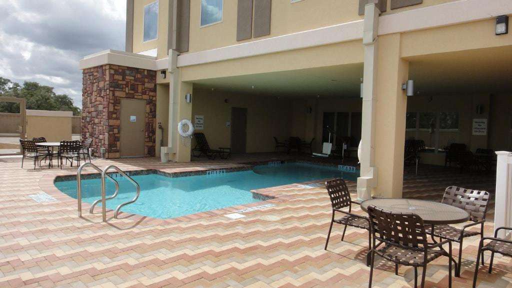 Outdoor pool with chevron paver deck, patio tables and covered seating area beside the hotel