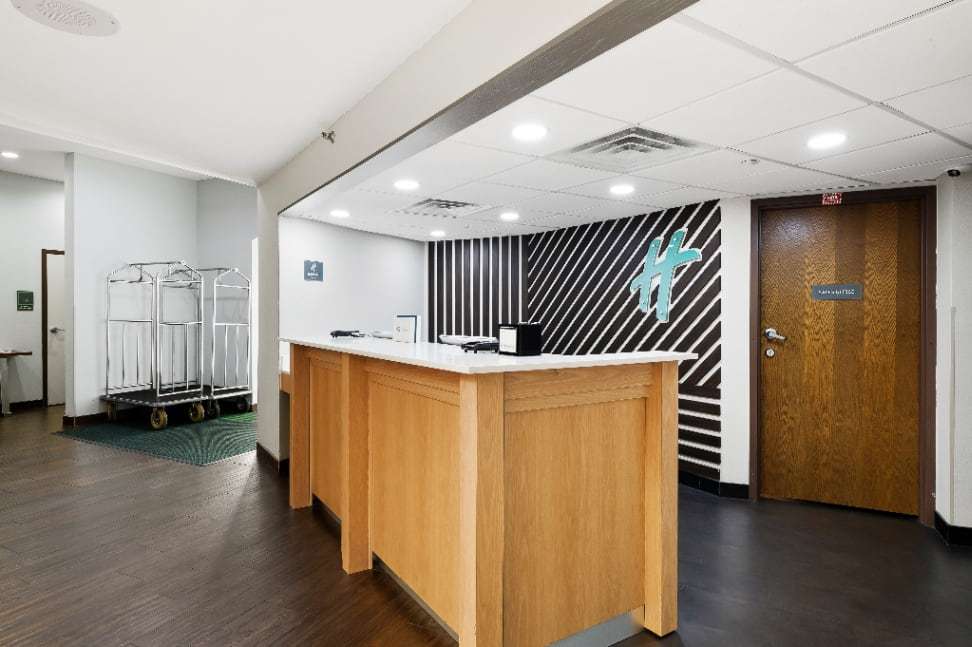 Front desk with wood counter, striped wall with the Holiday Inn logo and luggage carts