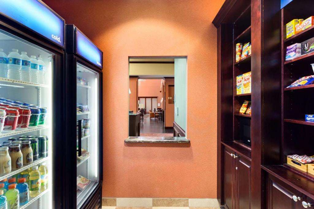 Lobby market with drink coolers and snack shelves beside a pass-through window