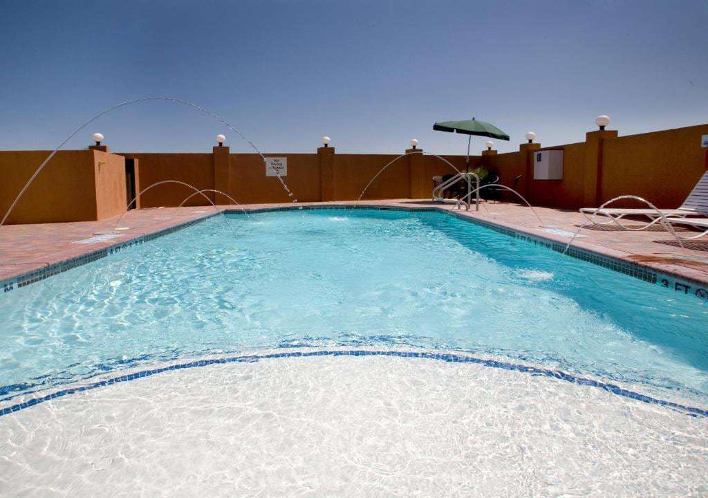 Walled outdoor pool with arching fountain jets, lounge chair and green patio umbrella