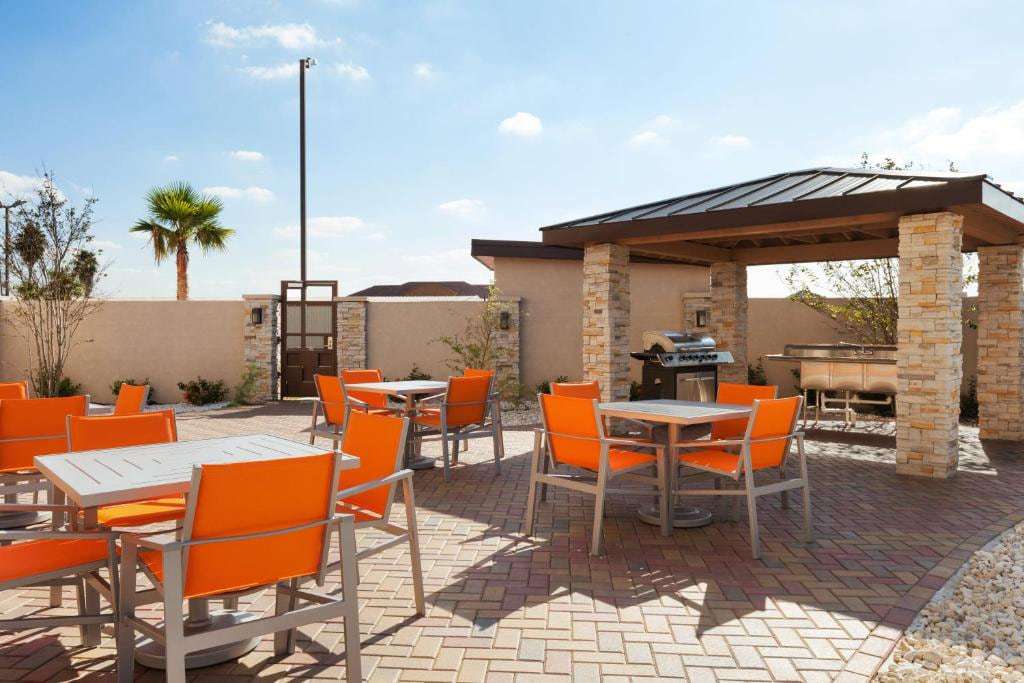 Outdoor patio with orange chairs, tables and a covered grill gazebo with stone columns