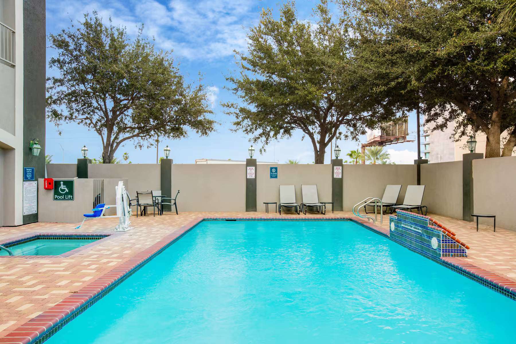 Outdoor pool with lounge chairs, accessible pool lift and shade trees