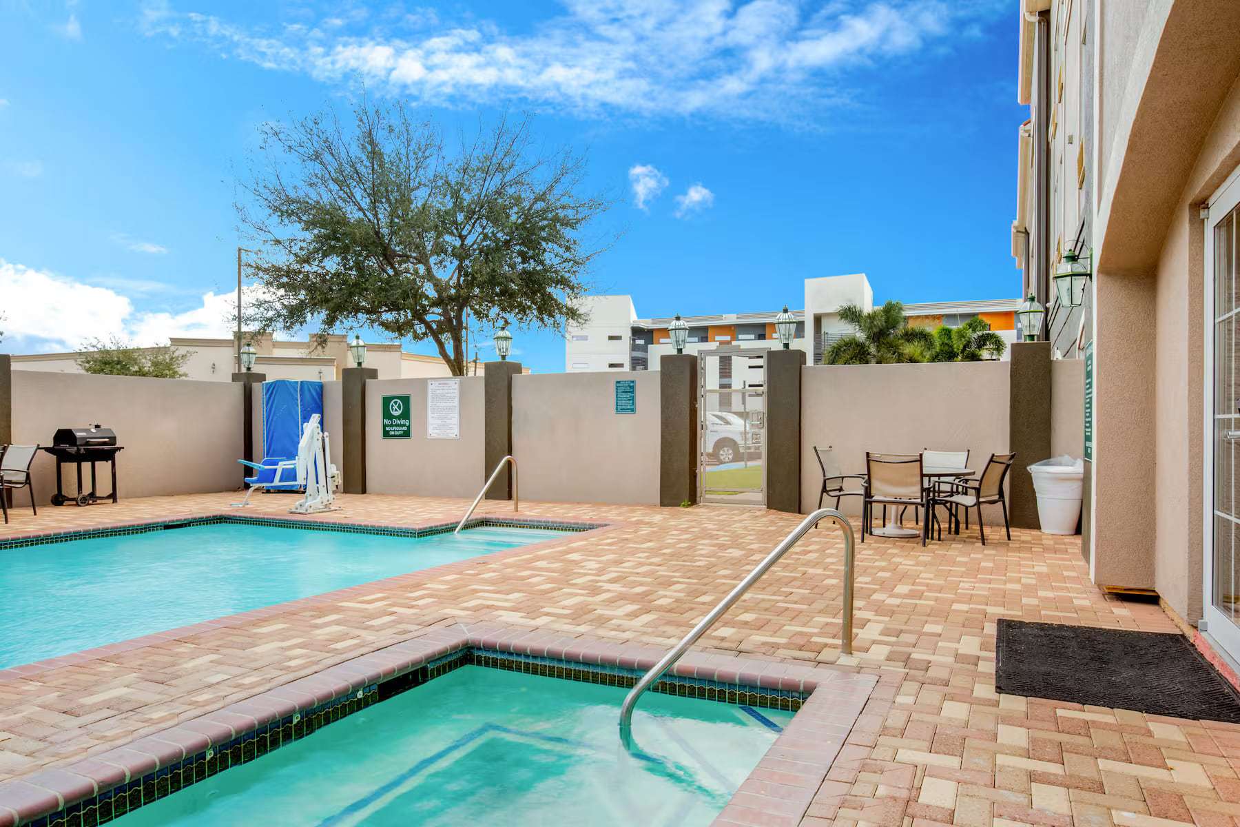 Outdoor hot tub next to the pool with patio table, chairs and barbecue grill
