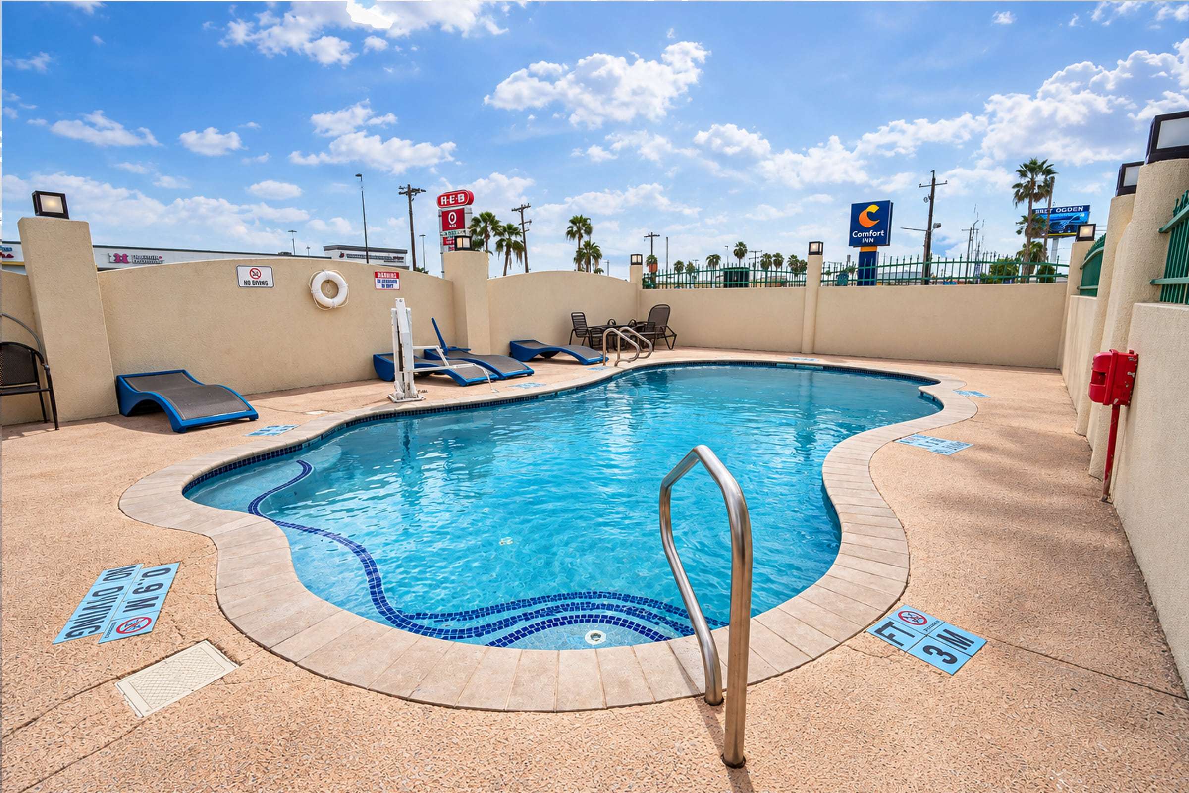 Outdoor pool with blue tile accents, a pool lift, blue lounge chairs and a walled sun deck