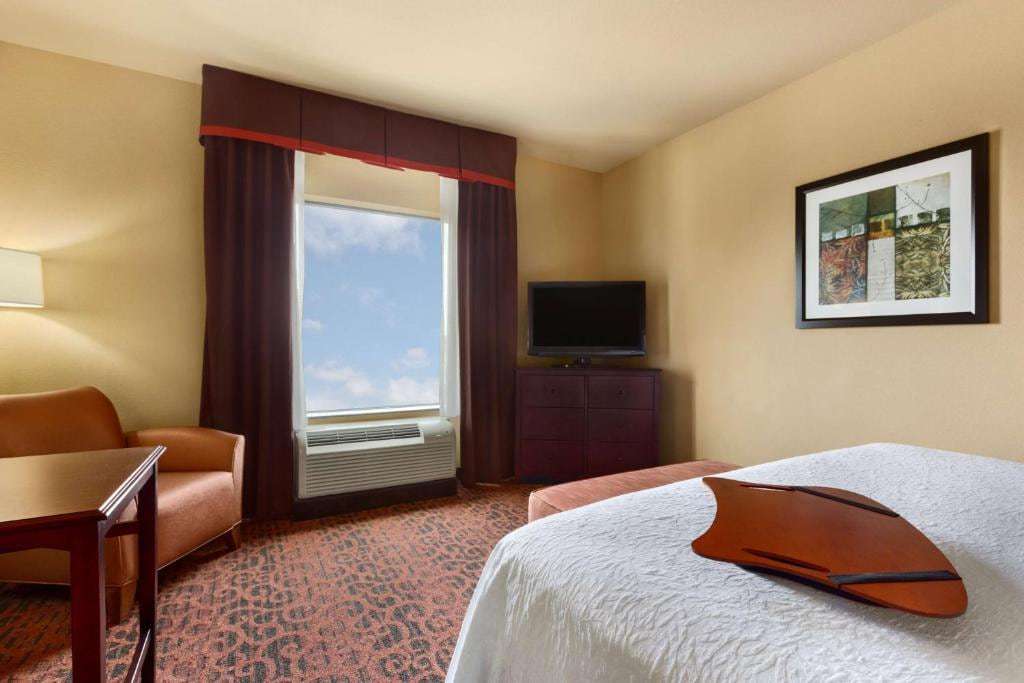 Guest room with one bed, armchair, desk and flat-screen TV on a dresser by the window
