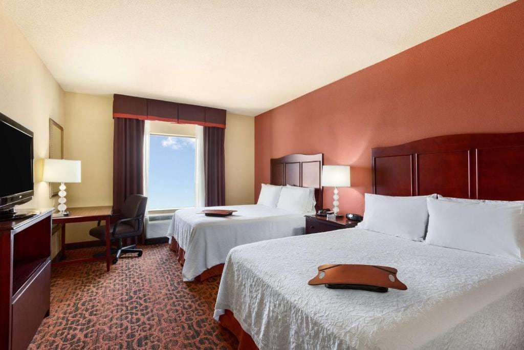 Room with two queen beds, red accent wall, work desk and flat-screen TV