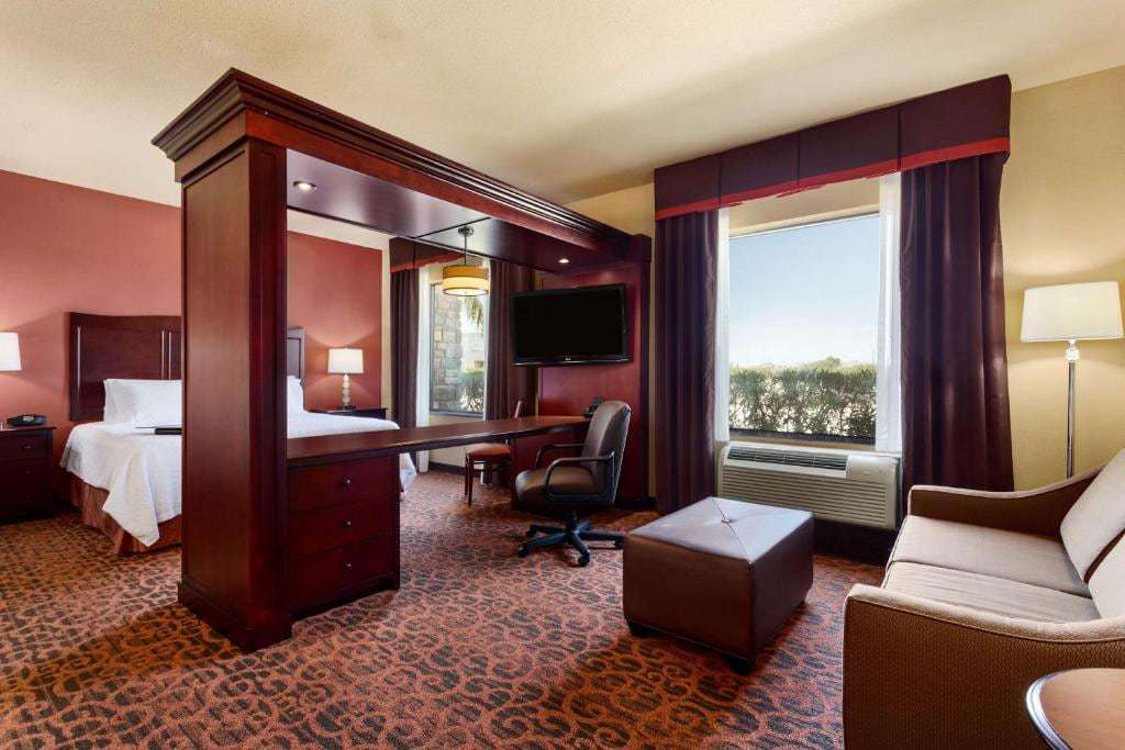 Studio suite with king bed behind a half-wall desk, wall-mounted TV, sofa and ottoman