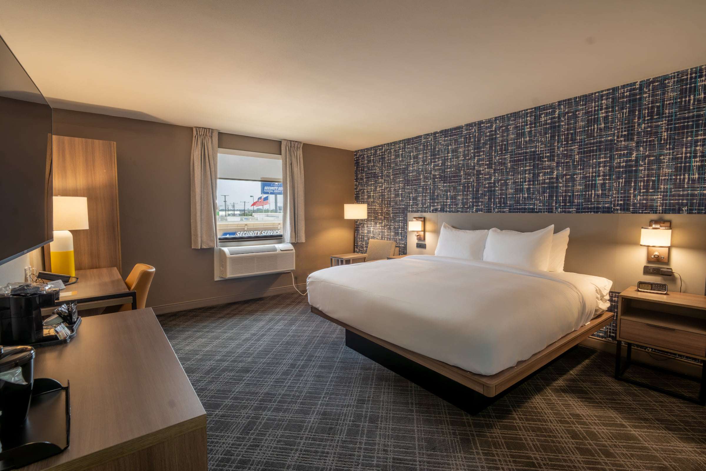 Guest room with a king bed, a desk with lamp and chair, and a window with an air-conditioning unit