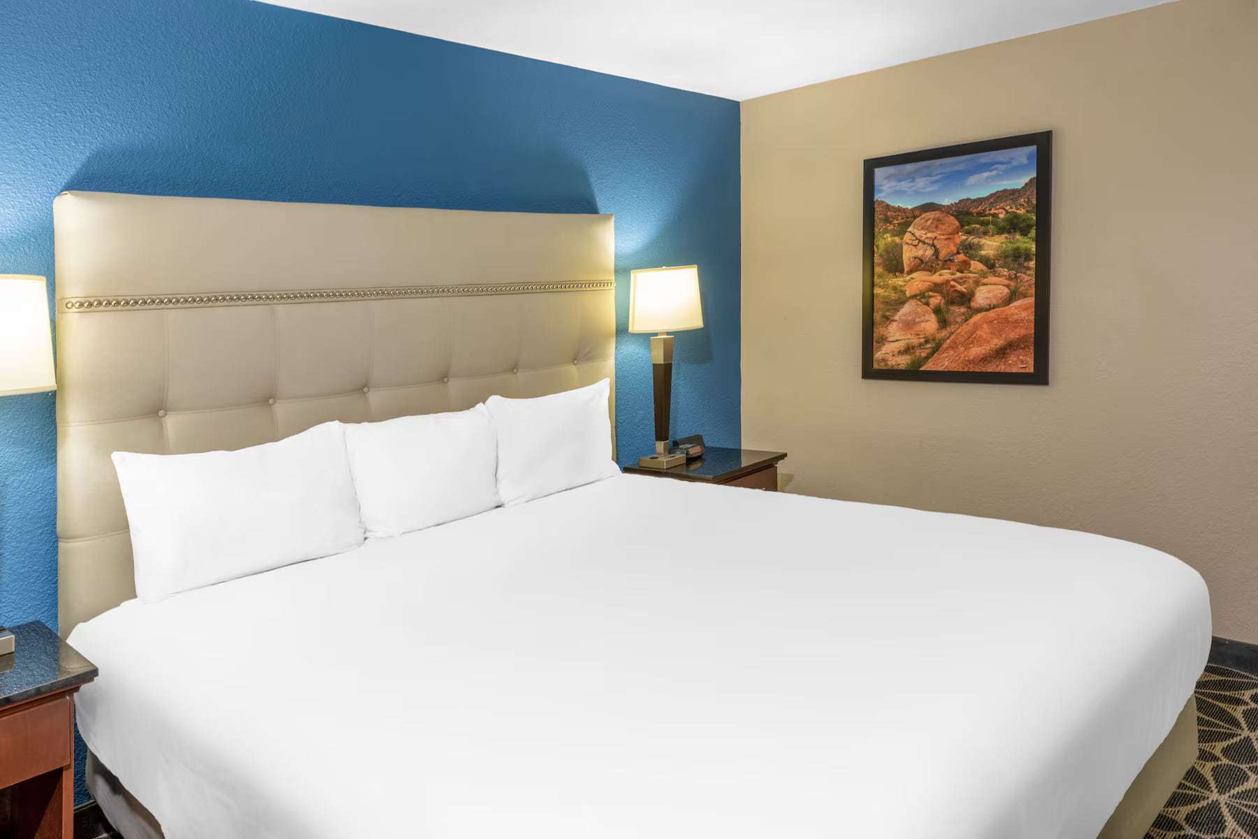 King bed with tufted headboard, bedside lamps and landscape artwork