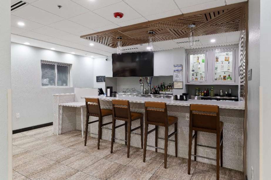 Lobby bar with four wood bar stools, wall TV and backlit display cabinets