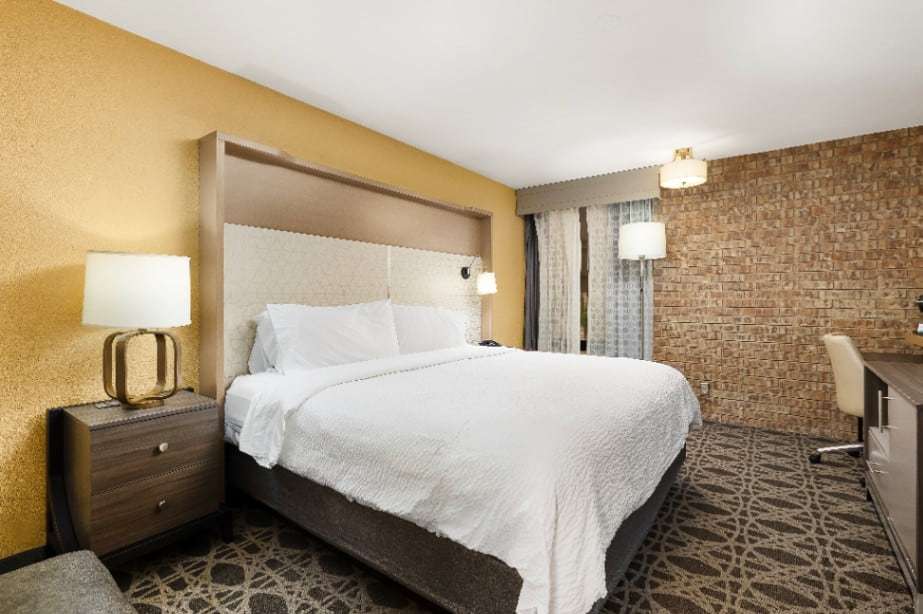 King bed with gold-base lamps, yellow accent wall, brick wall and work desk