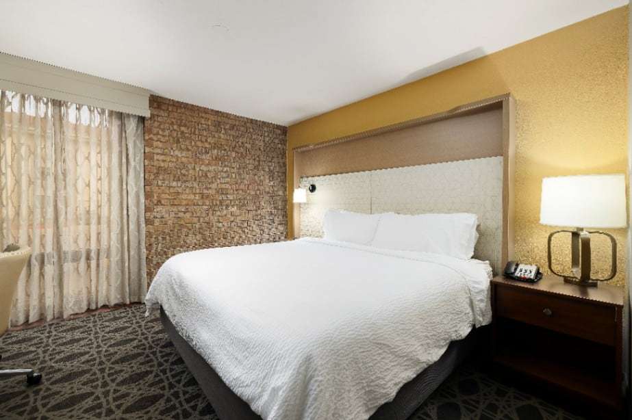 King bed with tall upholstered headboard, nightstand and sheer-curtained window