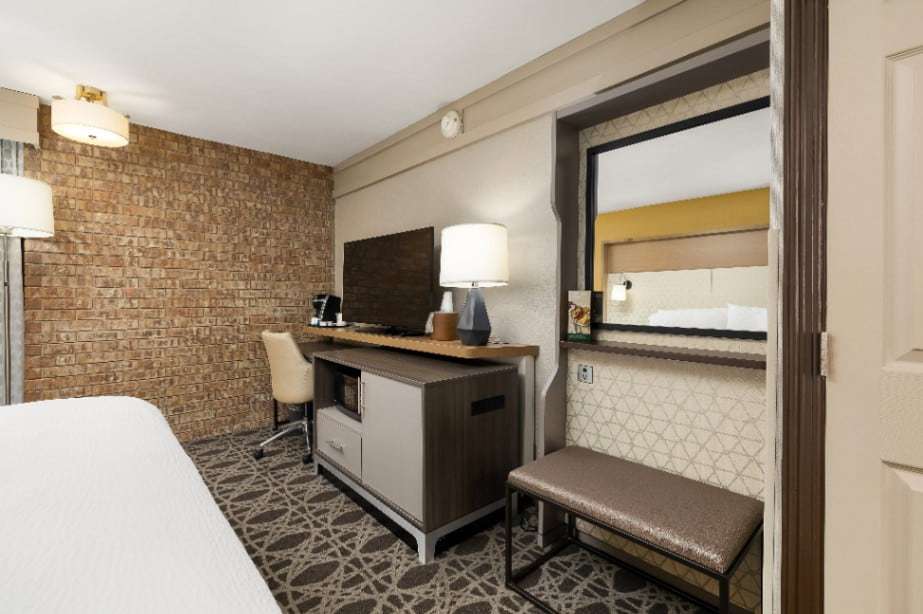 TV console with microwave and mini fridge, desk chair and mirror with bench in a guest room