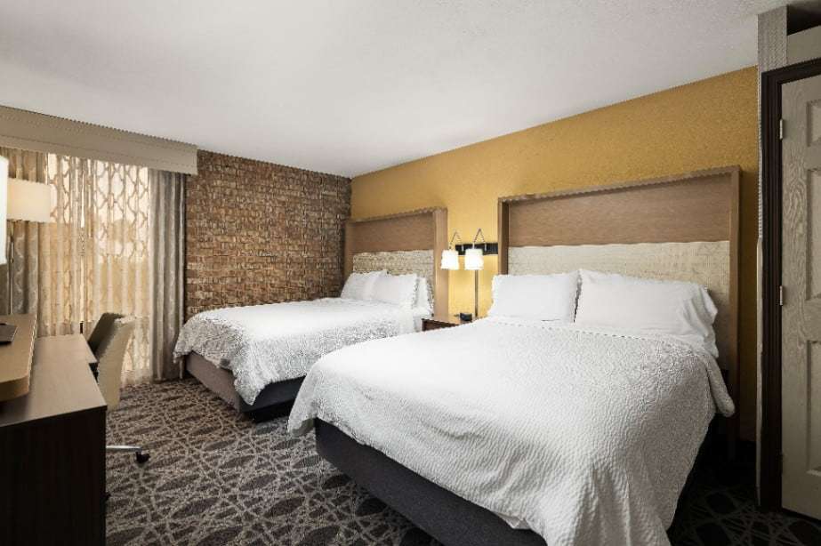 Room with two queen beds, yellow accent wall, brick wall and work desk