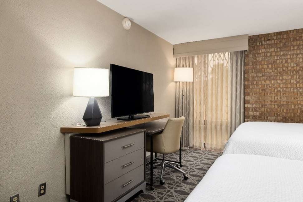 Work desk, TV dresser and floor lamp beside two beds in a guest room