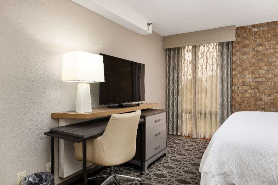 Work desk with ergonomic chair, TV and lamp next to the bed and window