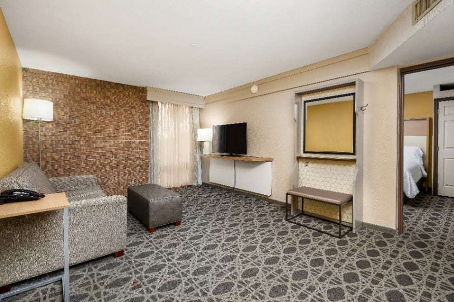 Suite living area with sofa, ottoman and TV, with the bedroom through the doorway