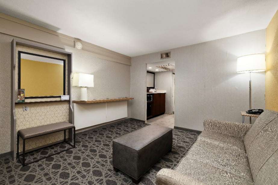 Suite living area with sofa, ottoman, mirror with bench and a view to the wet bar