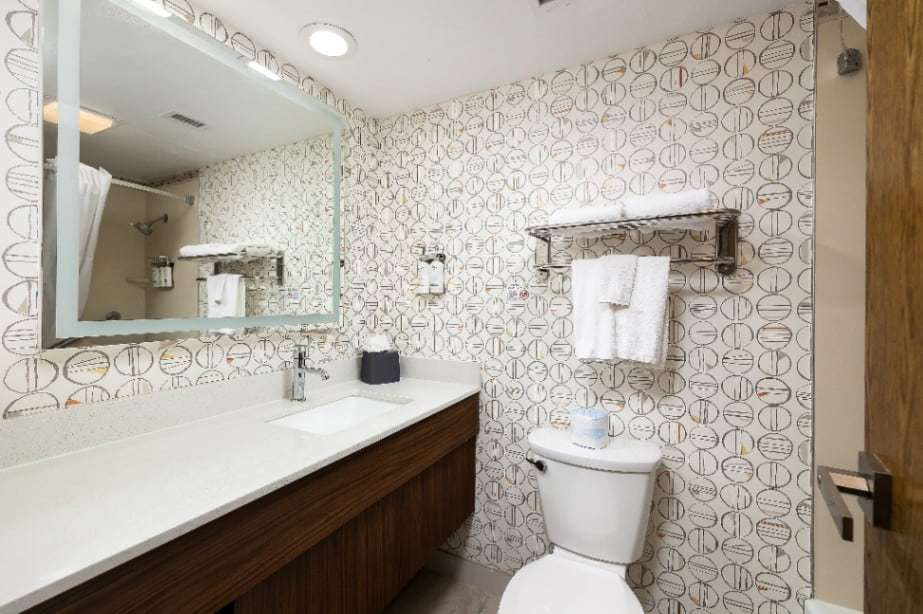 Bathroom with long vanity, large mirror, towel shelf and patterned wallpaper