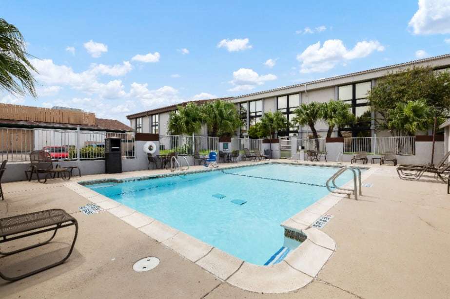 Outdoor pool with handrails, loungers and palm trees along the hotel wing