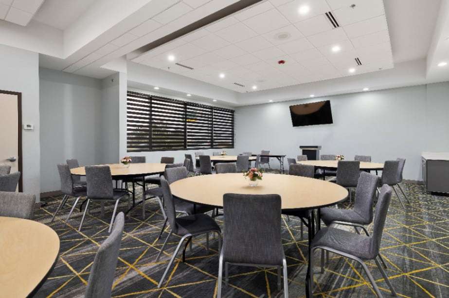 Meeting room with round tables, gray chairs, wall TV and shuttered windows