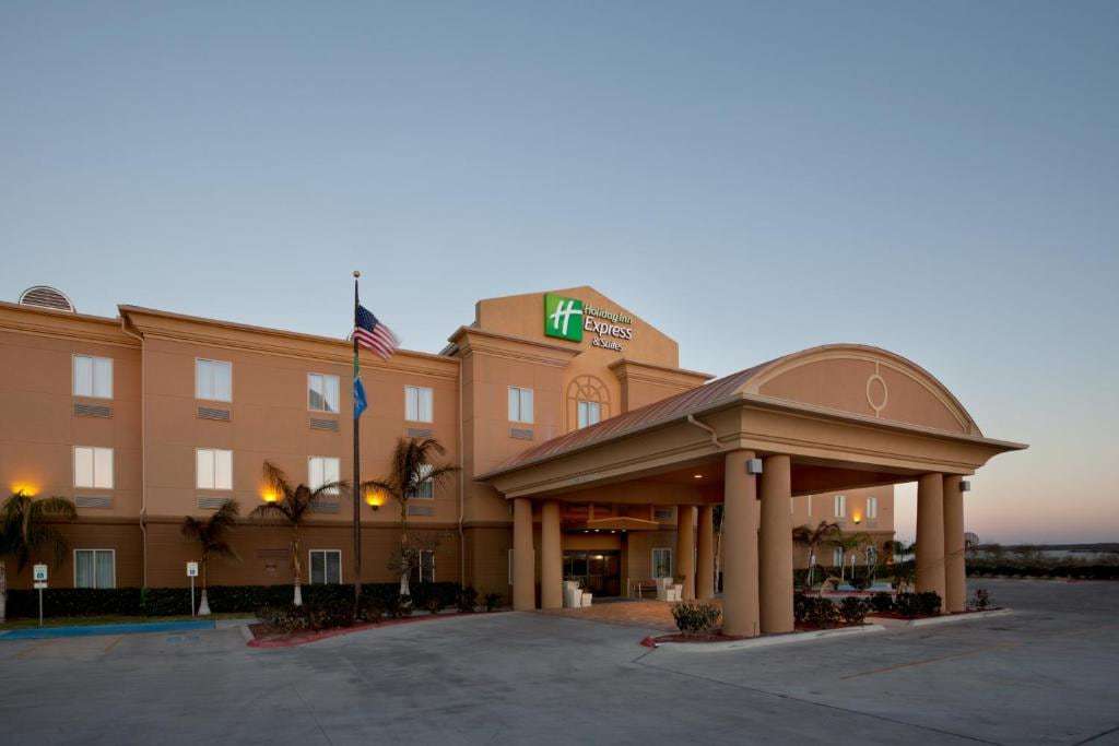 Holiday Inn Express & Suites Zapata at dusk with columned porte-cochere, flags and palm trees