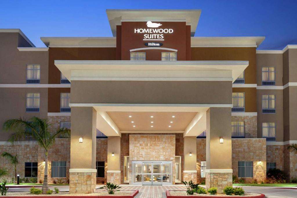 Homewood Suites by Hilton Harlingen entrance at dusk with lit sign, porte-cochere and palm trees